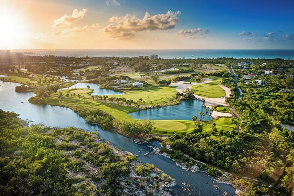 Ein Golfplatz mit einem See, umgeben von Grünflächen und Gebäuden.
