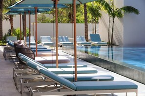 Ein Poolbereich mit Liegestühlen und Sonnenschirmen, umgeben von Palmen.