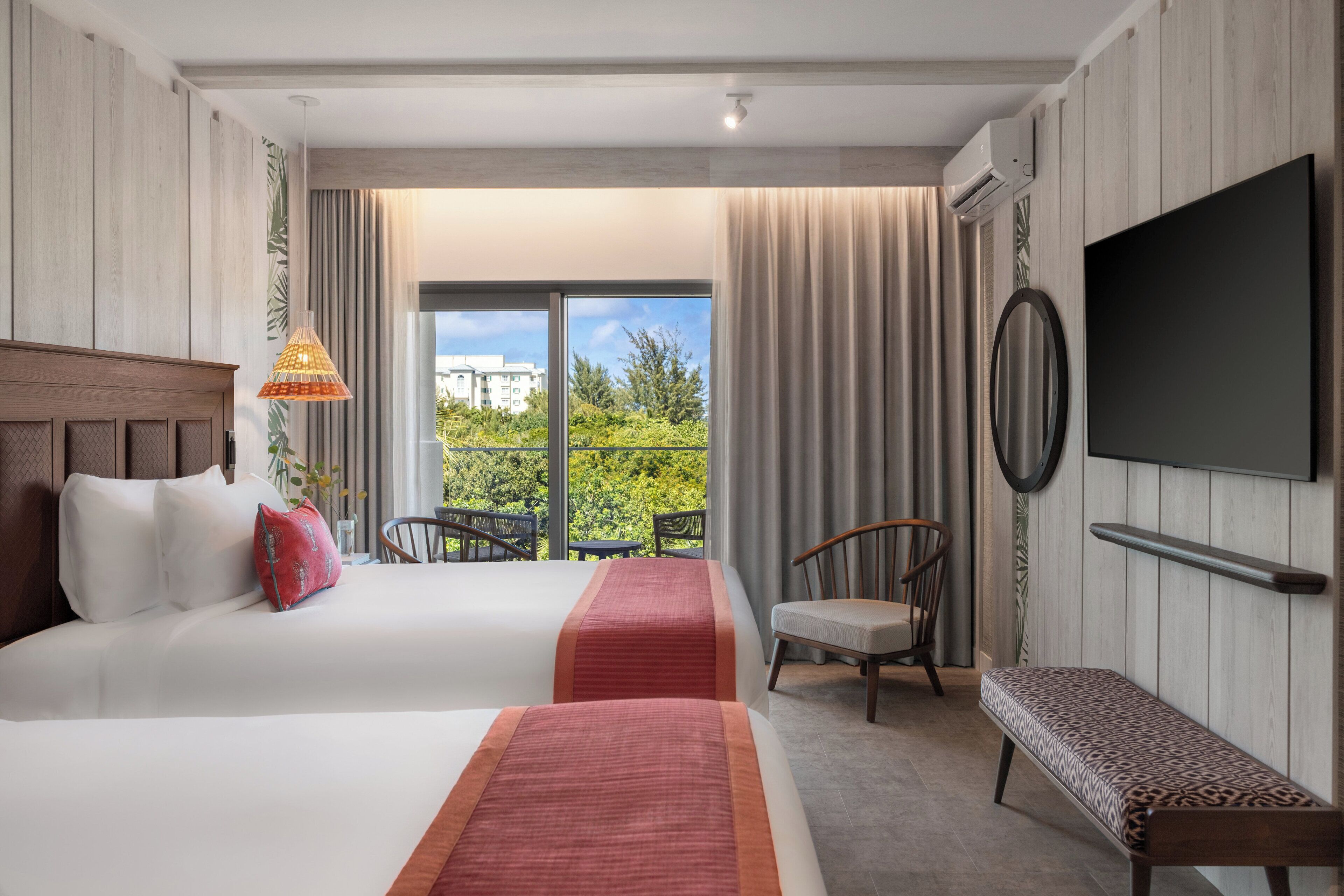 Habitación de hotel con dos camas, un banco, un televisor y un balcón con vistas.