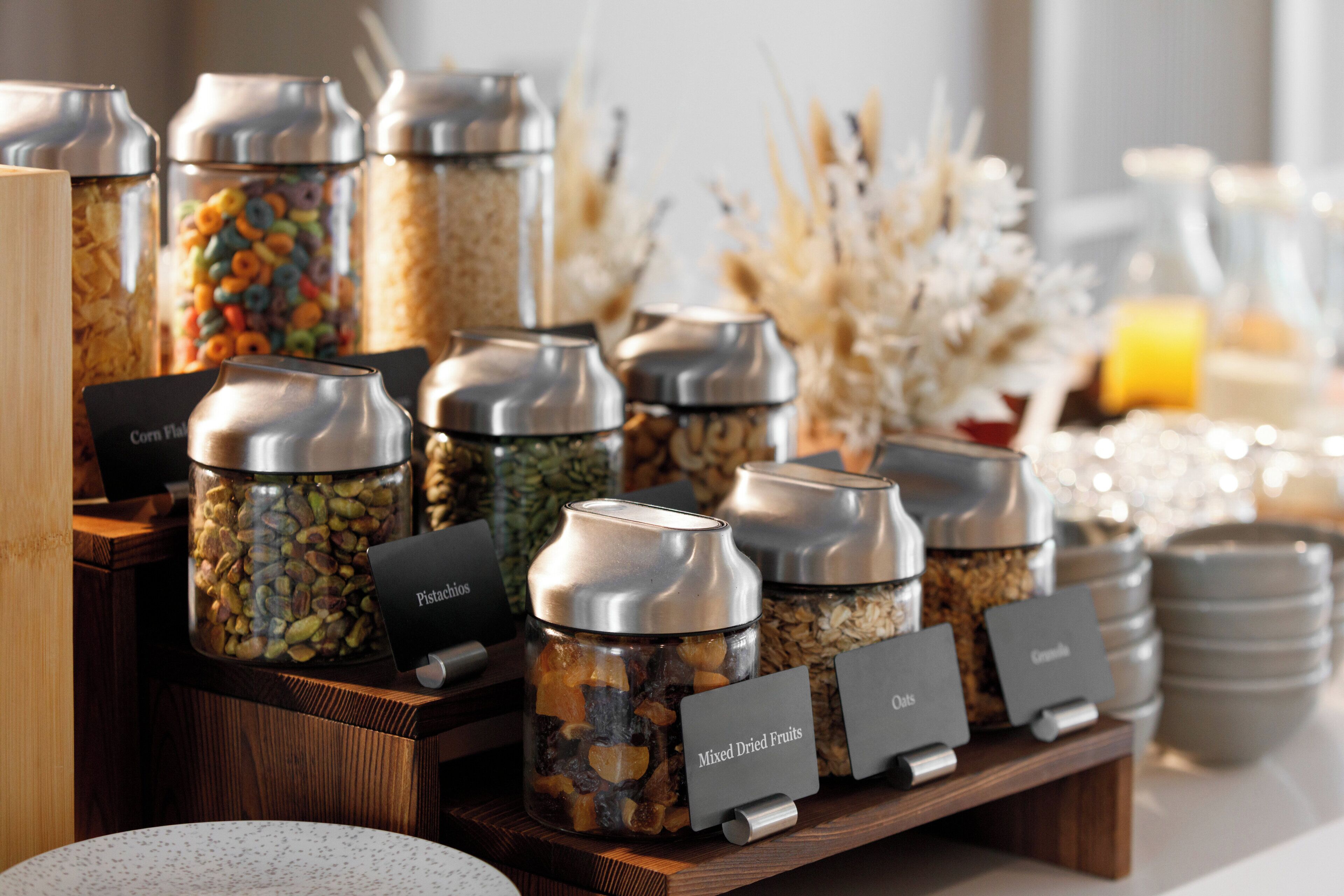 A breakfast buffet with labeled containers of mixed dried fruits, pistachios, and oats.