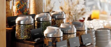 A breakfast buffet with labeled containers of mixed dried fruits, pistachios, and oats.