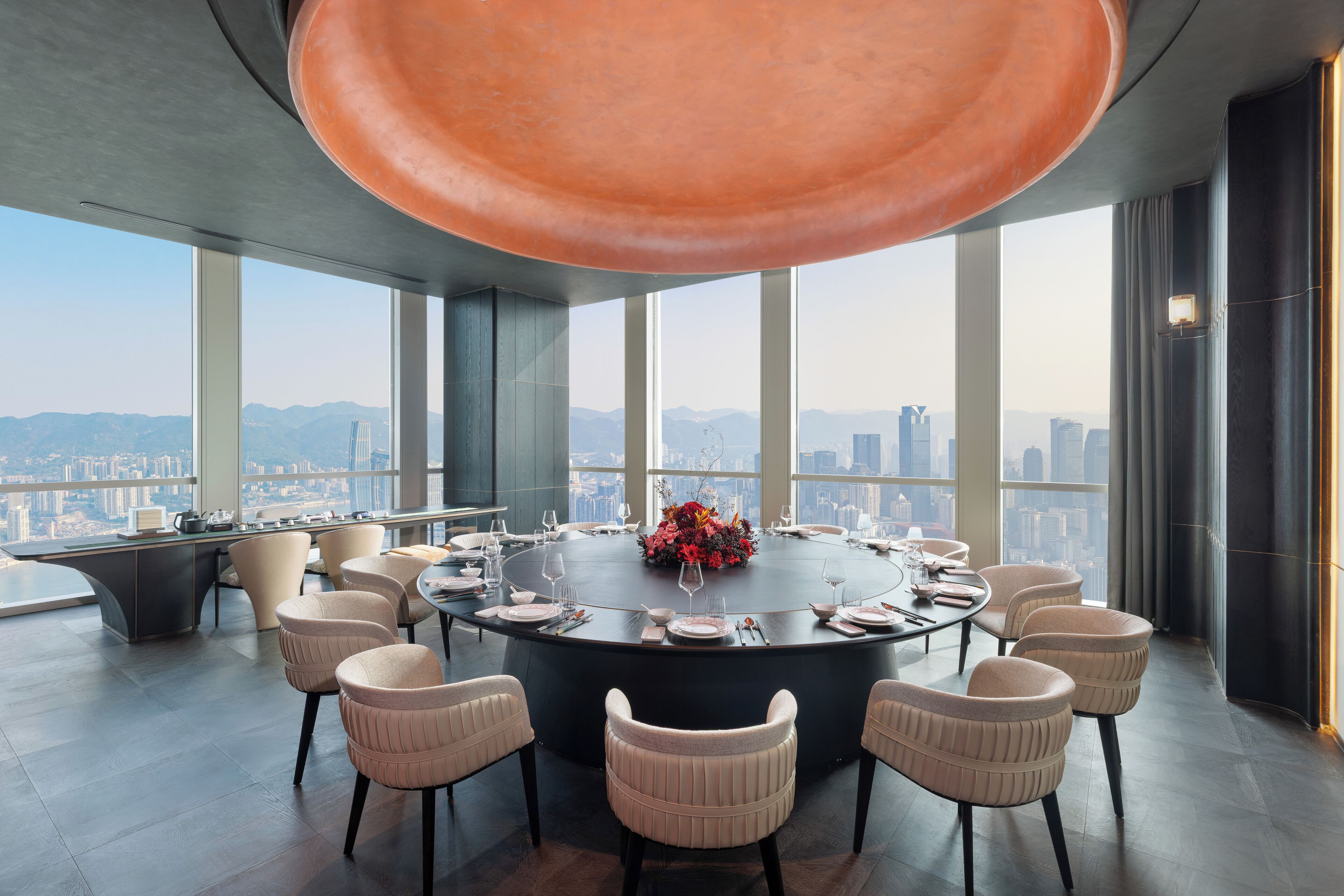 Sala de conferências moderna com uma mesa redonda, cadeiras bege e vista para a cidade.