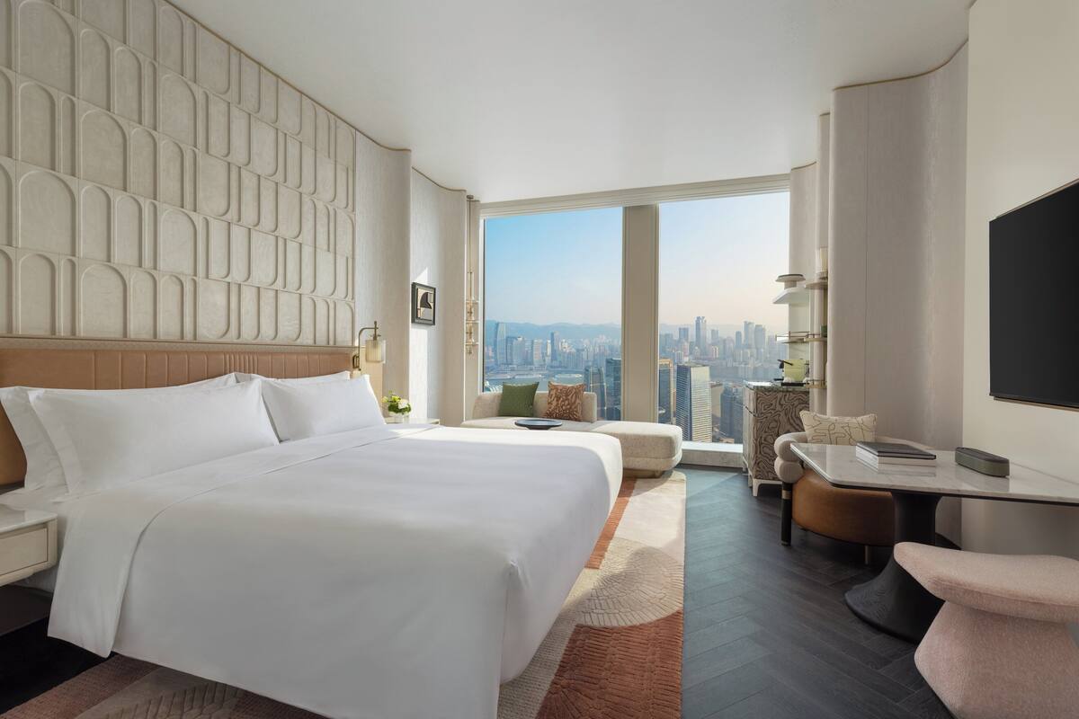 Una habitación de hotel moderna con una cama grande, una zona de estar con vistas a la ciudad y un televisor de pantalla plana.