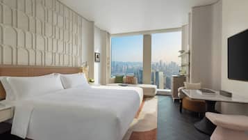 A modern hotel room with a large bed, a seating area with a view of the city, and a flat-screen TV.