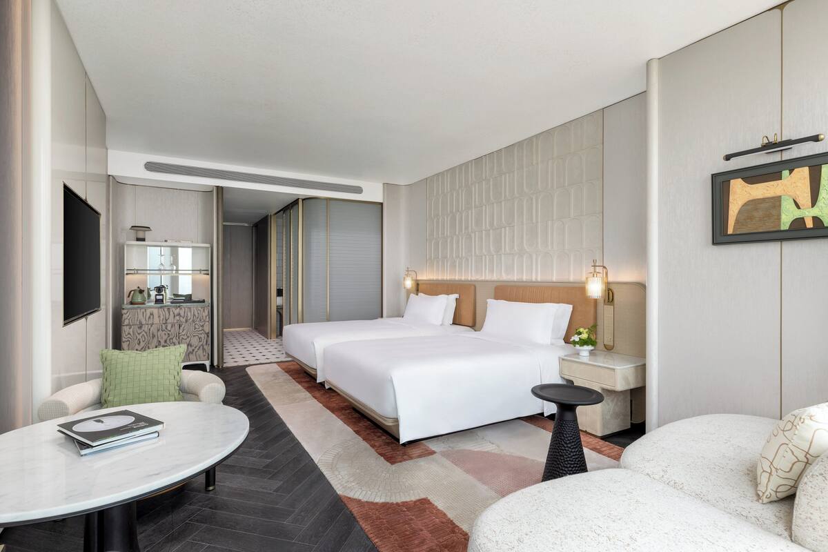 Una habitación de hotel moderna con una cama grande, una zona de estar con una mesa y vistas al pasillo.