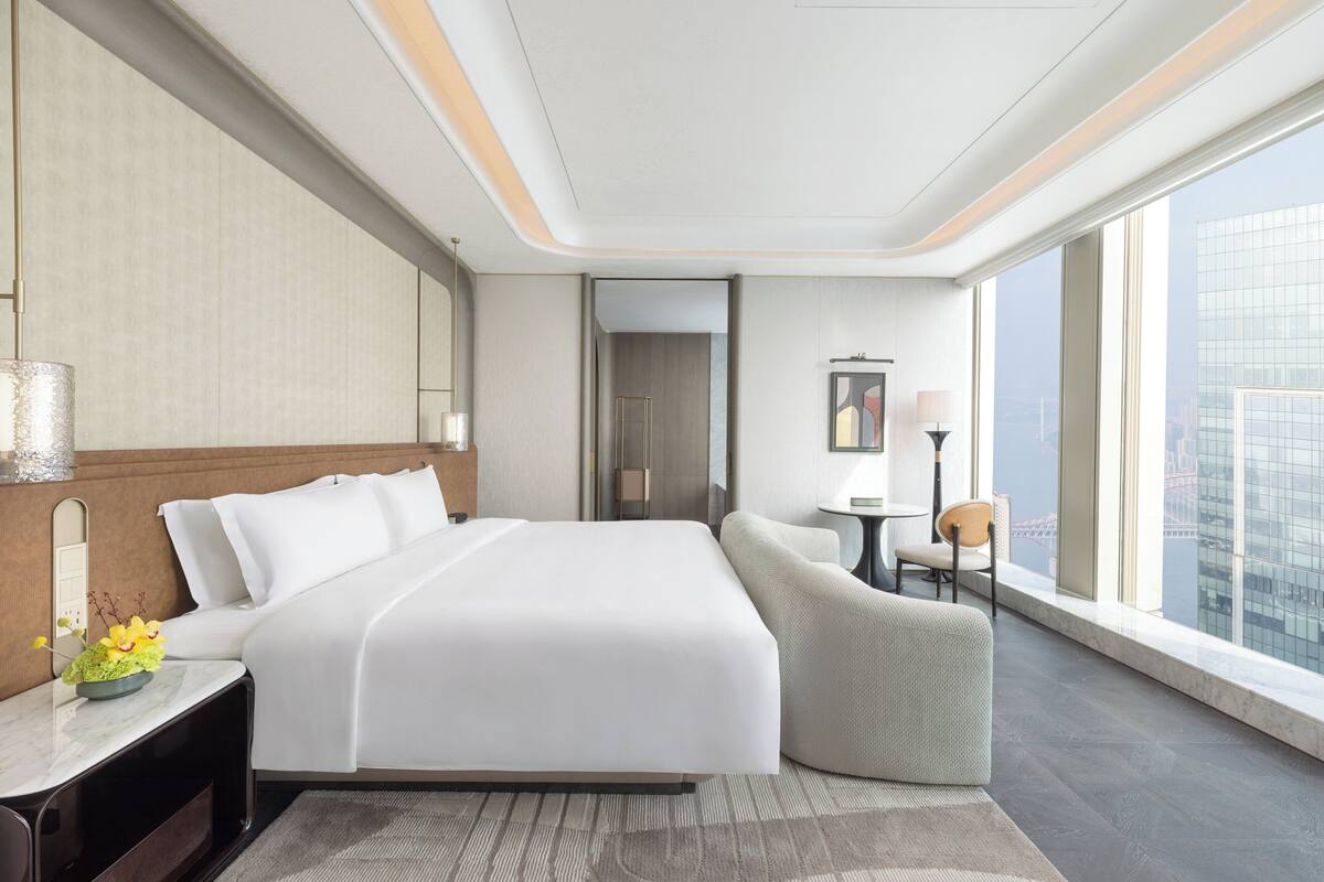 Una habitación de hotel moderna con una cama grande, un área de descanso y vistas a la ciudad.