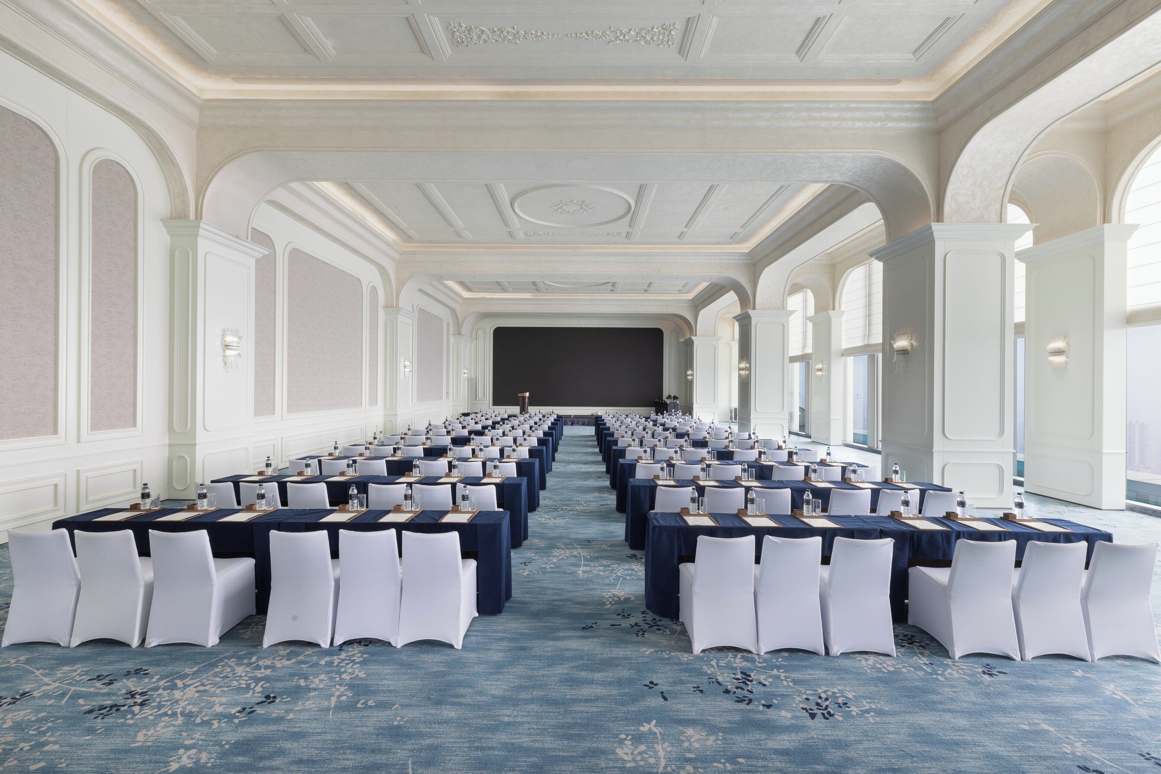 A conference room with rows of tables and chairs, a carpeted floor, and a large window on one side.