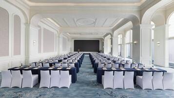 A conference room with rows of tables and chairs, a carpeted floor, and a large window on one side.
