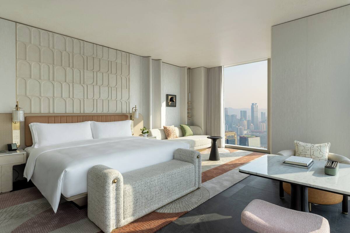 Habitación de hotel moderna con una cama grande, un sofá, una mesita y vistas a la ciudad.