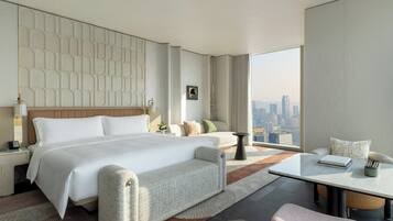 A modern hotel room with a large bed, a sofa, a small table, and a view of the city.