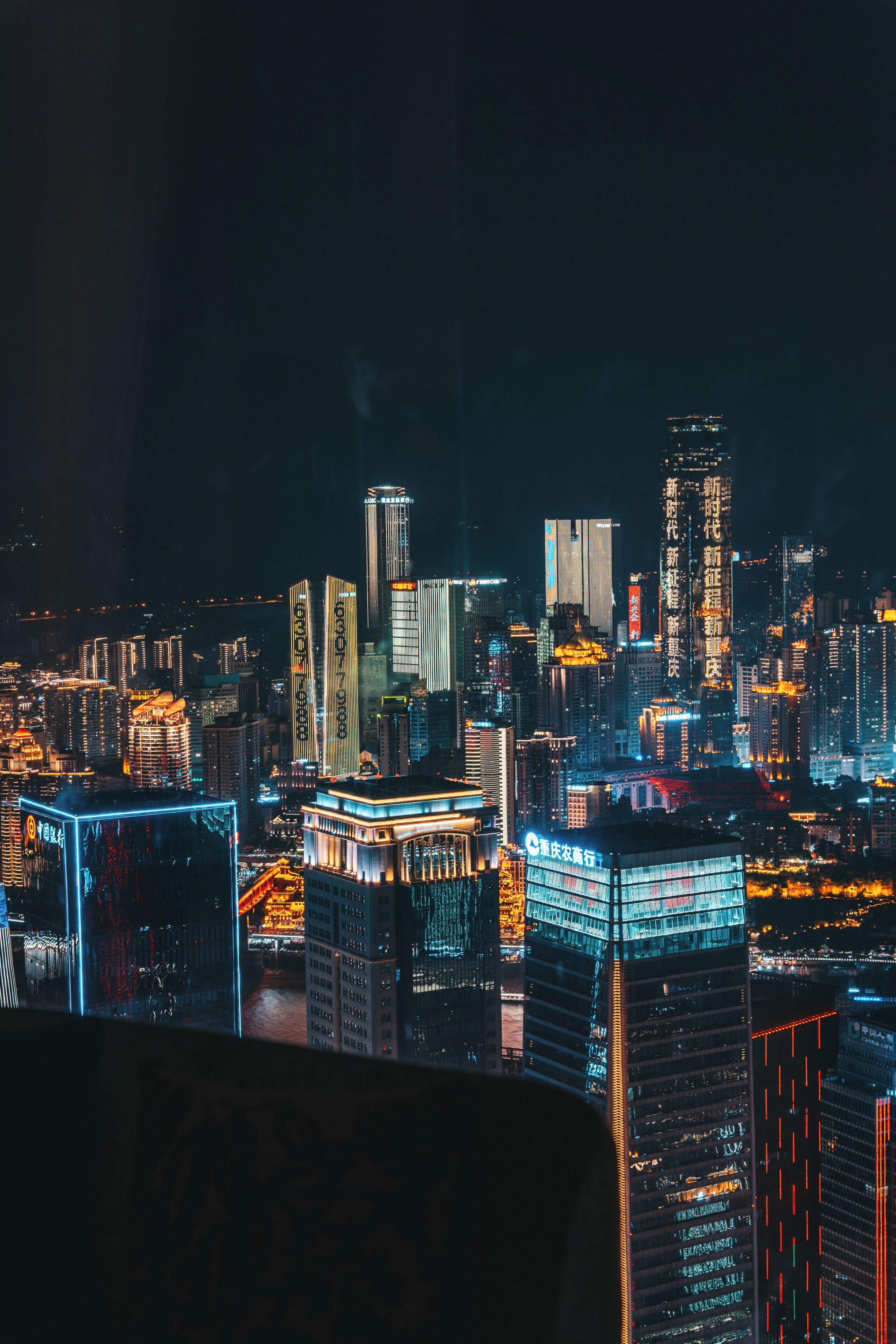 A nighttime cityscape with illuminated skyscrapers and a river.