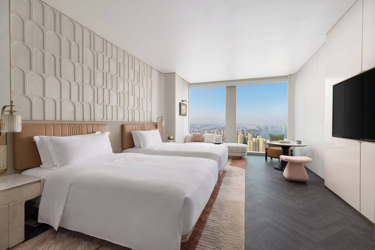 Una habitación de hotel moderna con dos camas, vistas a la ciudad, un televisor de pantalla plana y un área de comedor.