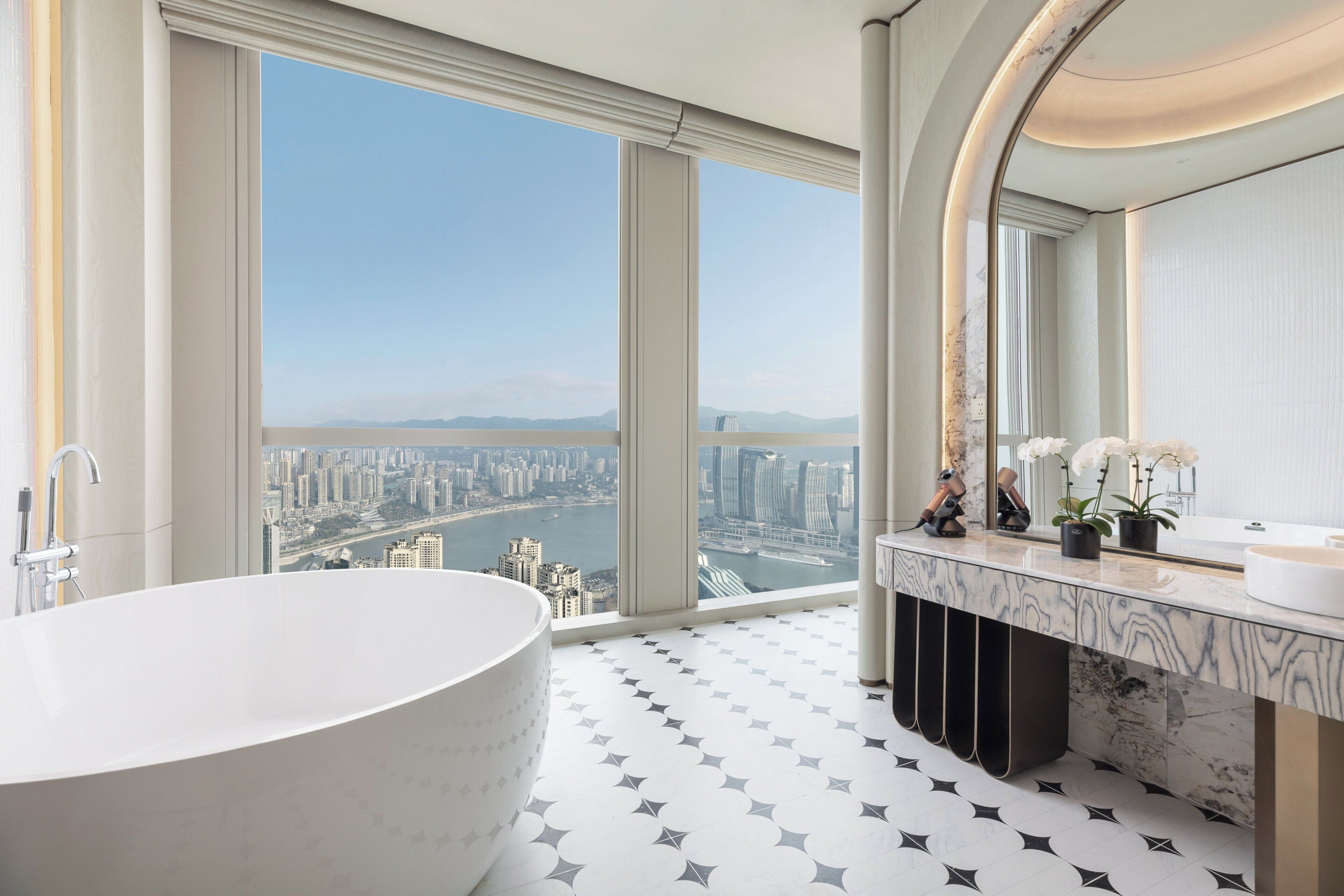 A modern bathroom with a large bathtub, a vanity with a mirror, and a view of a cityscape through large windows.