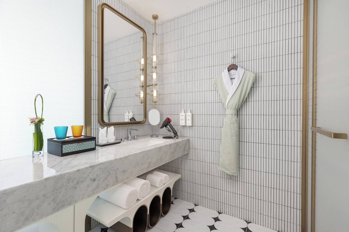 Un baño moderno con lavamanos de mármol, un espejo grande y un perchero para toallas.