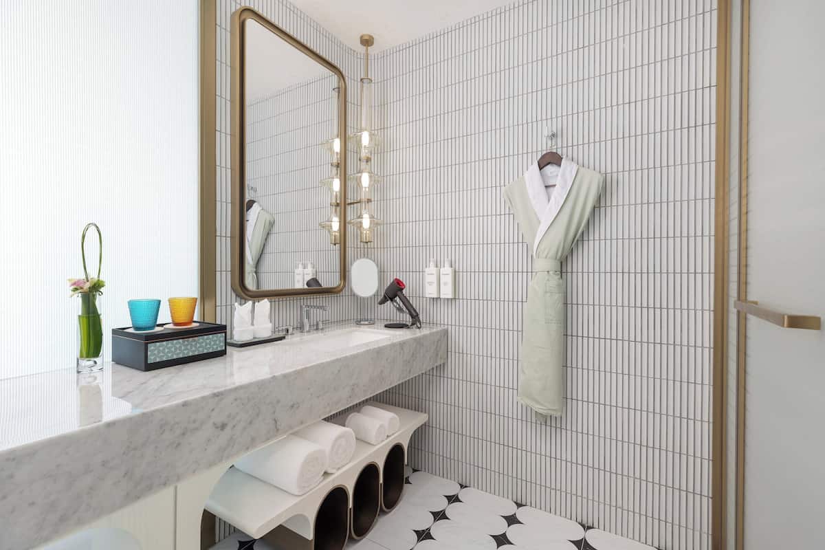 Un baño moderno con lavamanos de mármol, un espejo grande y un perchero para toallas.