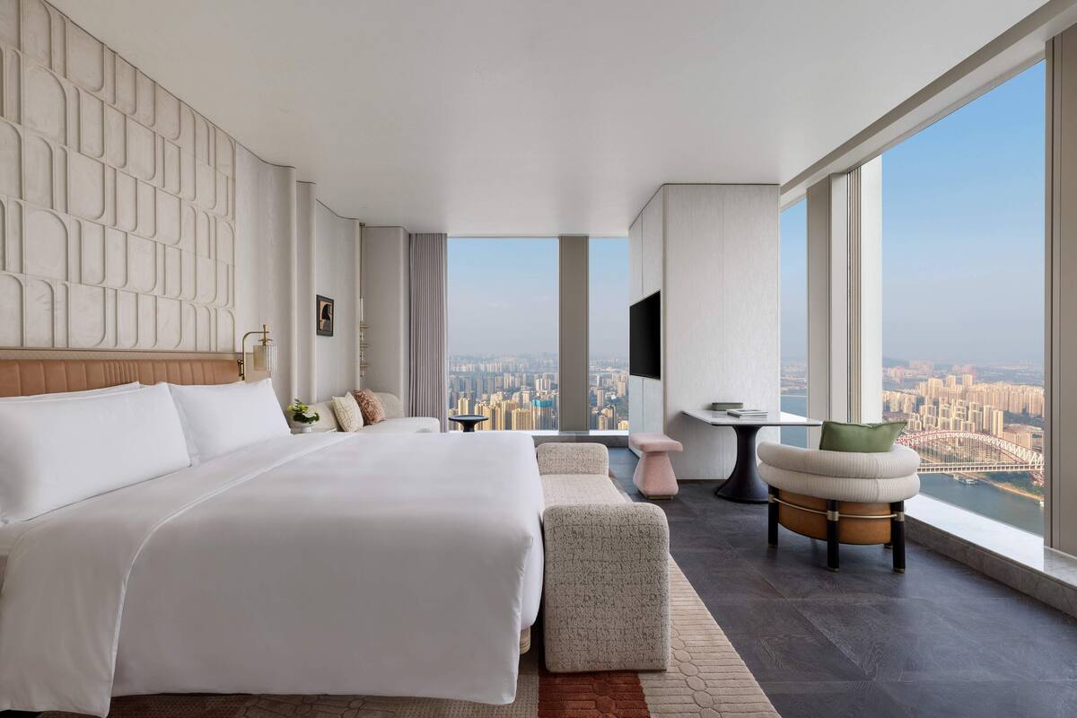 Una habitación de hotel moderna con una cama grande, una zona de estar y vistas a la ciudad.