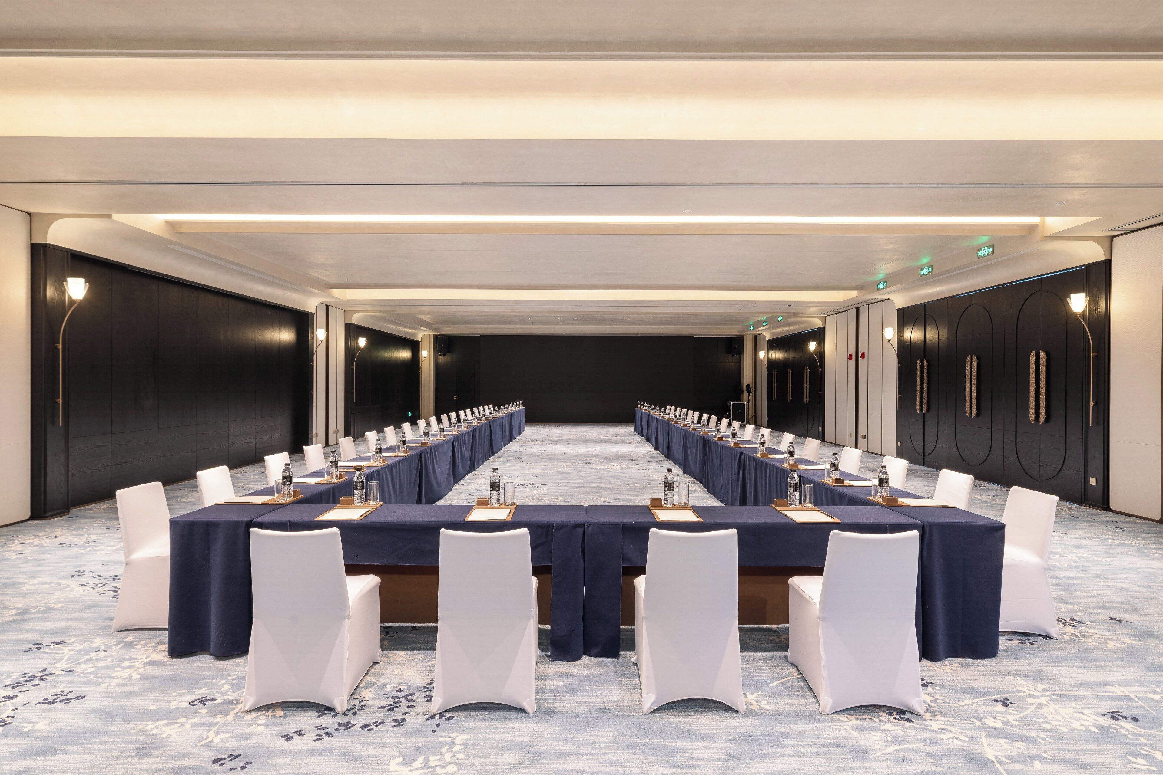 A conference room with a long table, white chairs, and a carpeted floor.