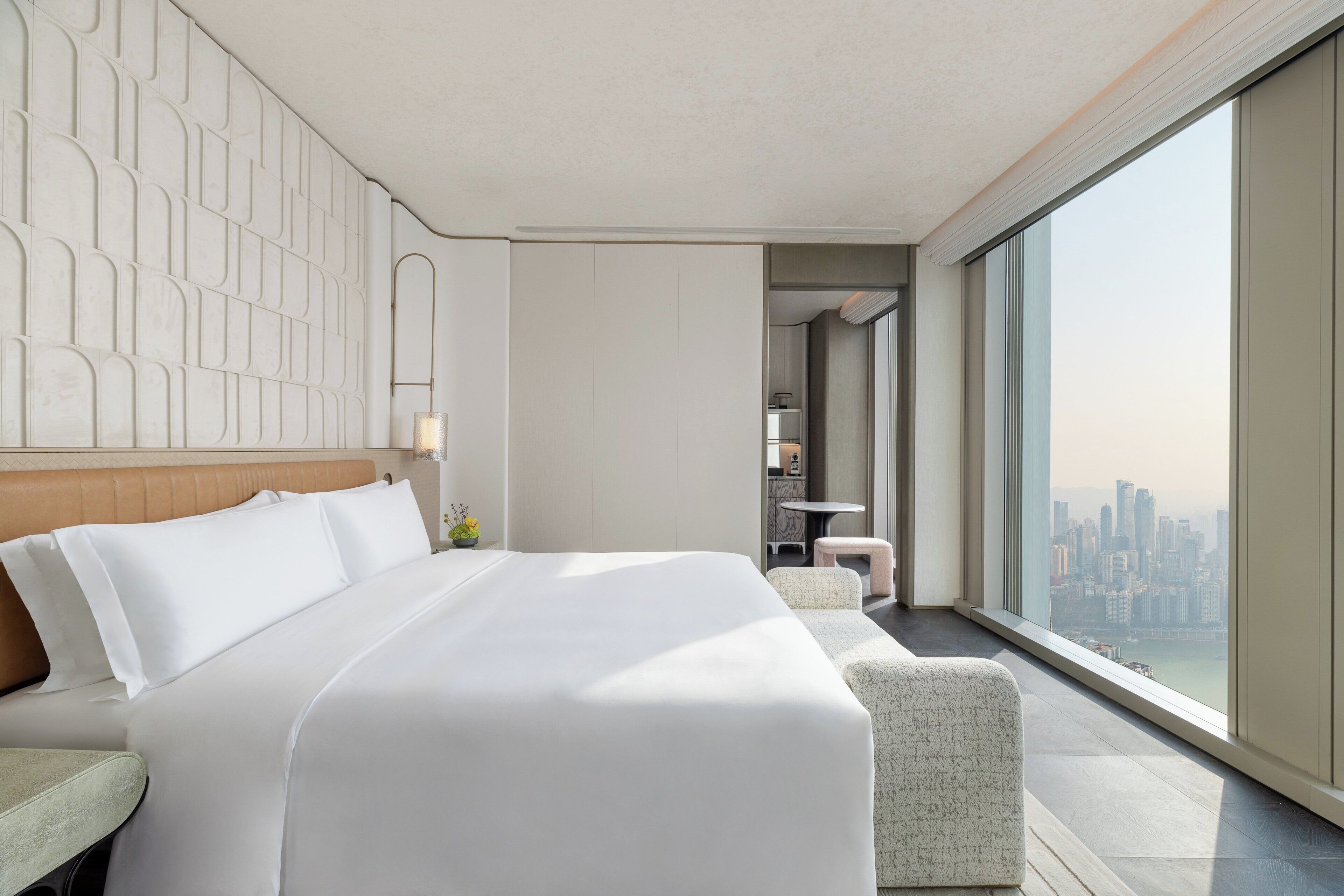A modern hotel room with a large bed, a seating area, and a city view.
