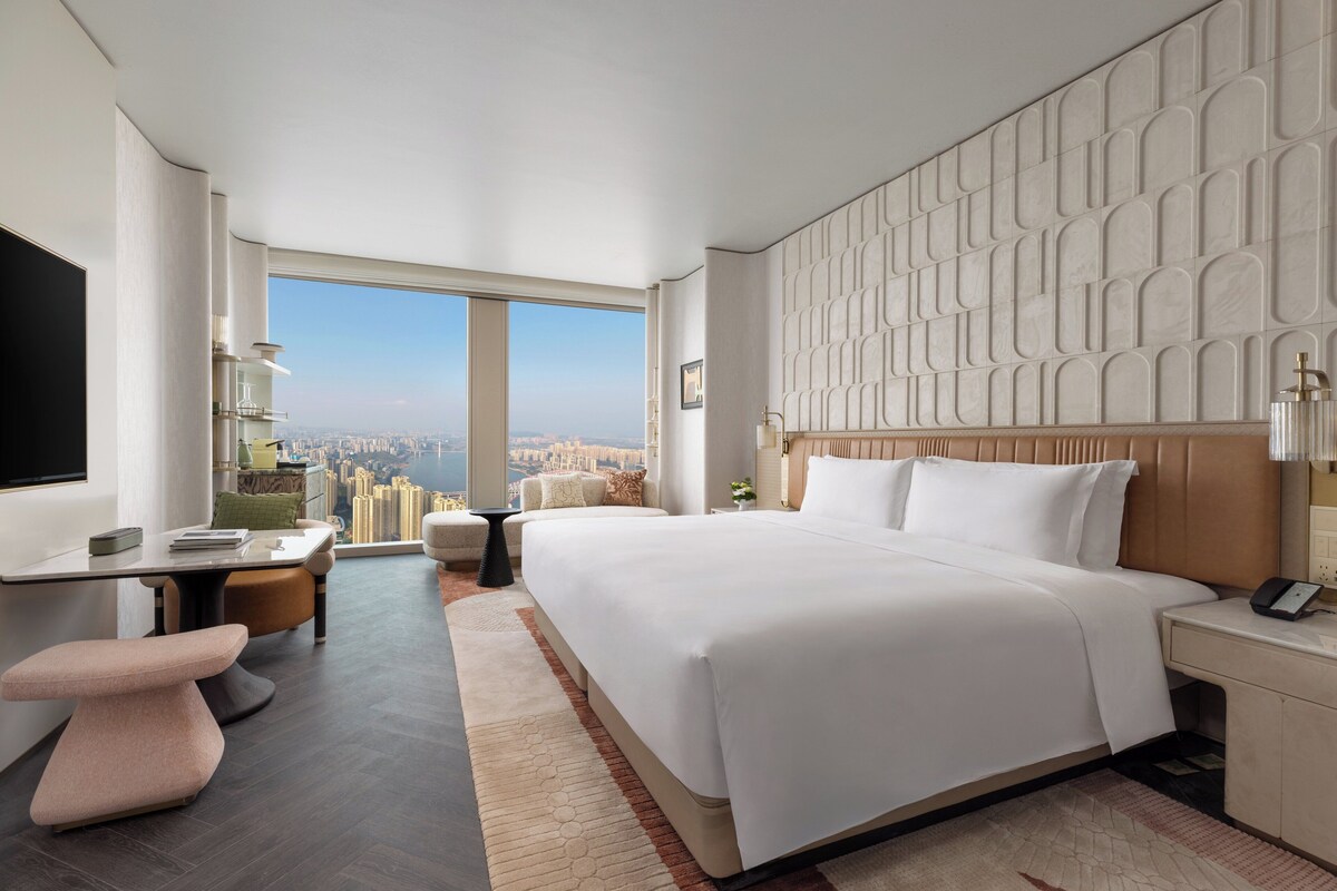 Un moderno cuarto de hotel con una cama grande, un escritorio y vista a la ciudad.
