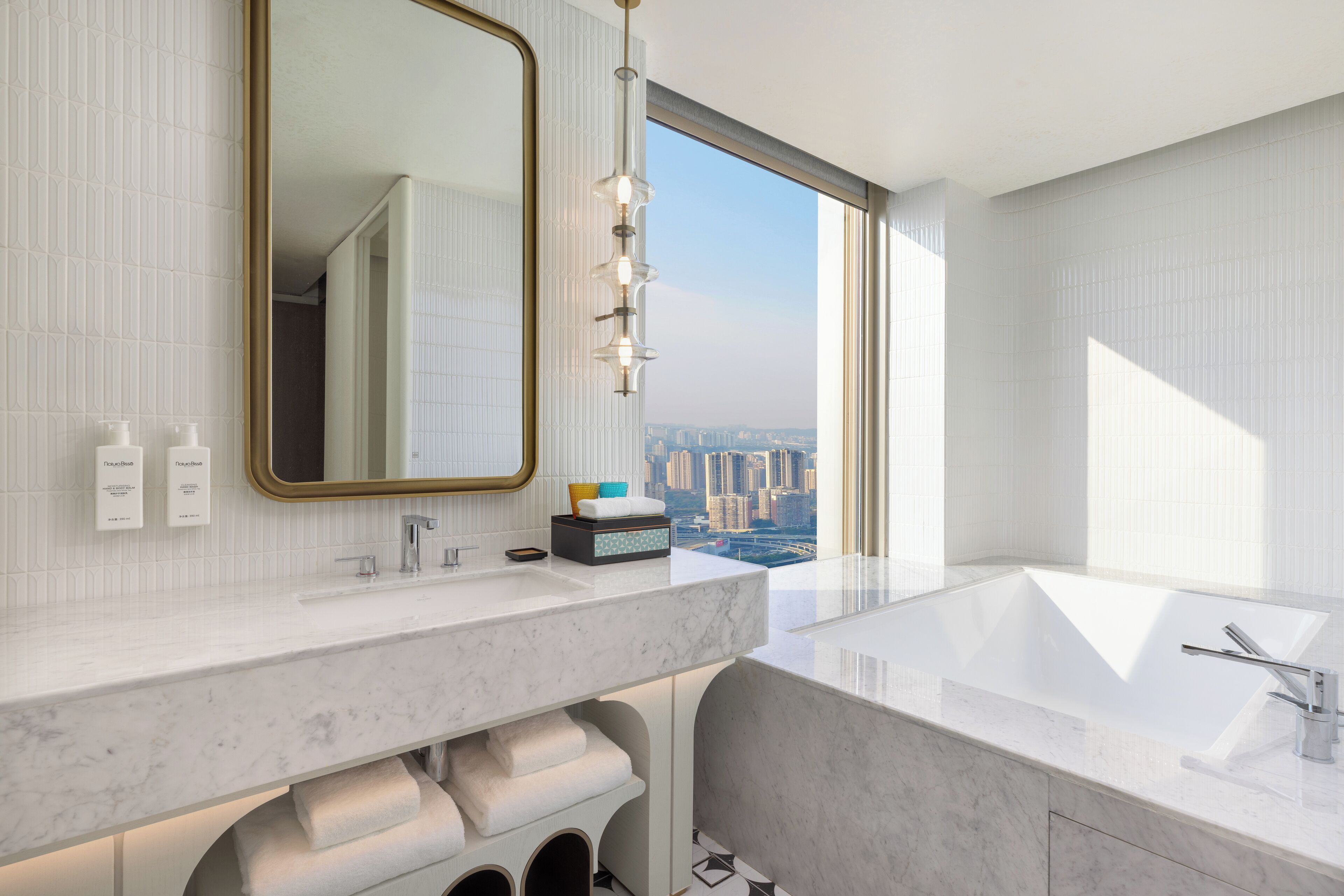 A modern bathroom with a large window, a marble sink, and a vanity with toiletries.