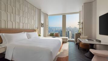 Una habitación de hotel moderna con una cama grande, un espacio de descanso con vista a la ciudad y un televisor de pantalla plana.