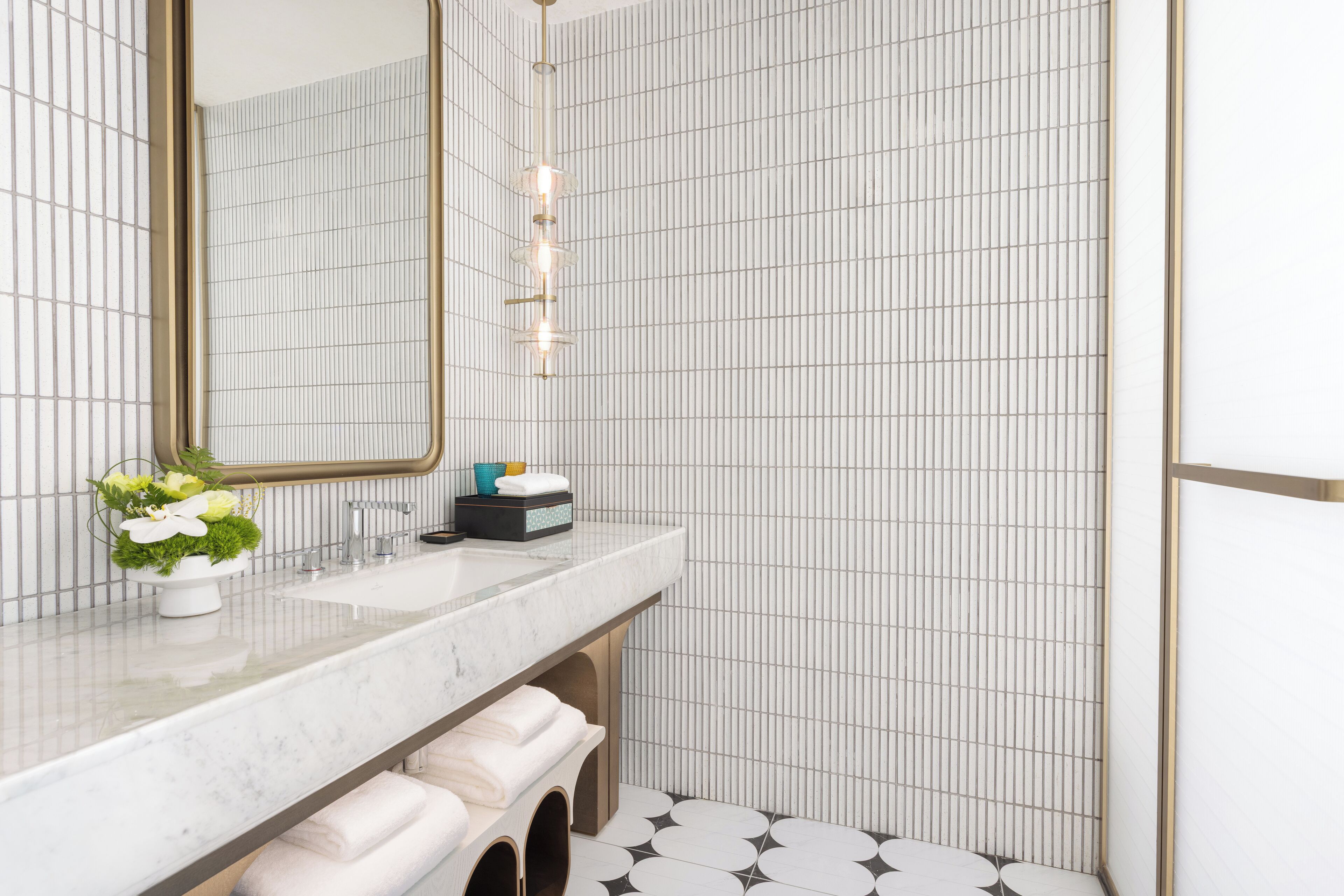 Une salle de bain moderne avec un lavabo en marbre, un grand miroir et un mur orné d’un motif à carreaux.