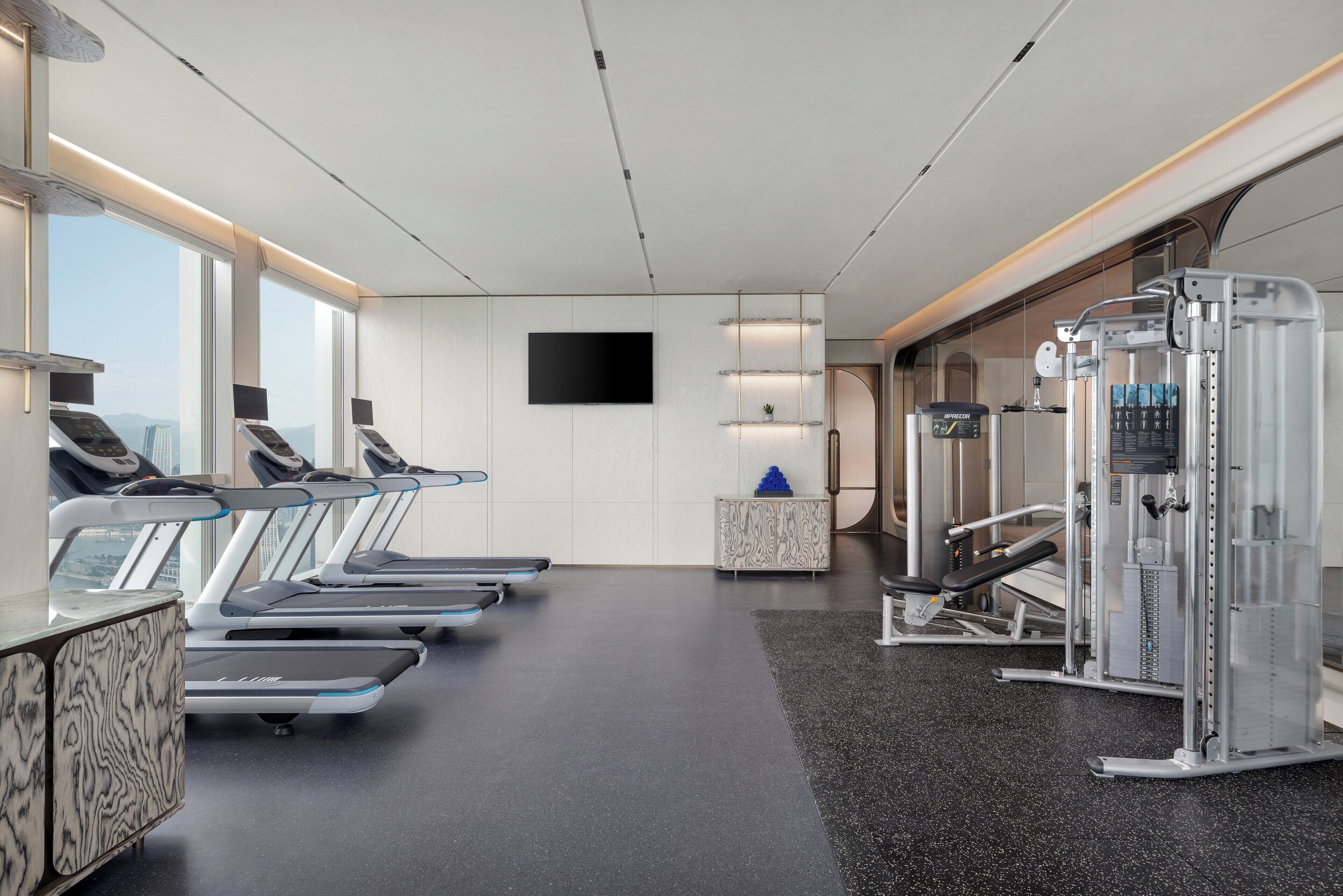 A modern fitness center with treadmills, a weight machine, and a TV screen on the wall.