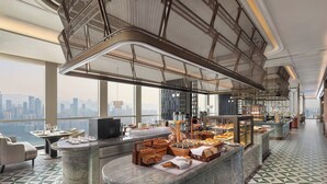 A high-rise hotel lobby with a city view, a marble reception desk, and a buffet area.