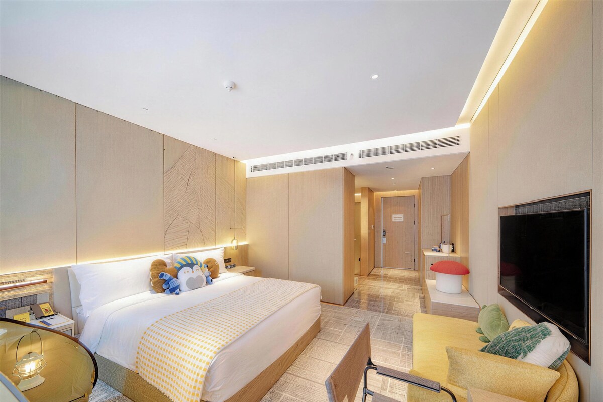 A modern hotel room with a large bed, a flat-screen TV, a desk, and a chair.