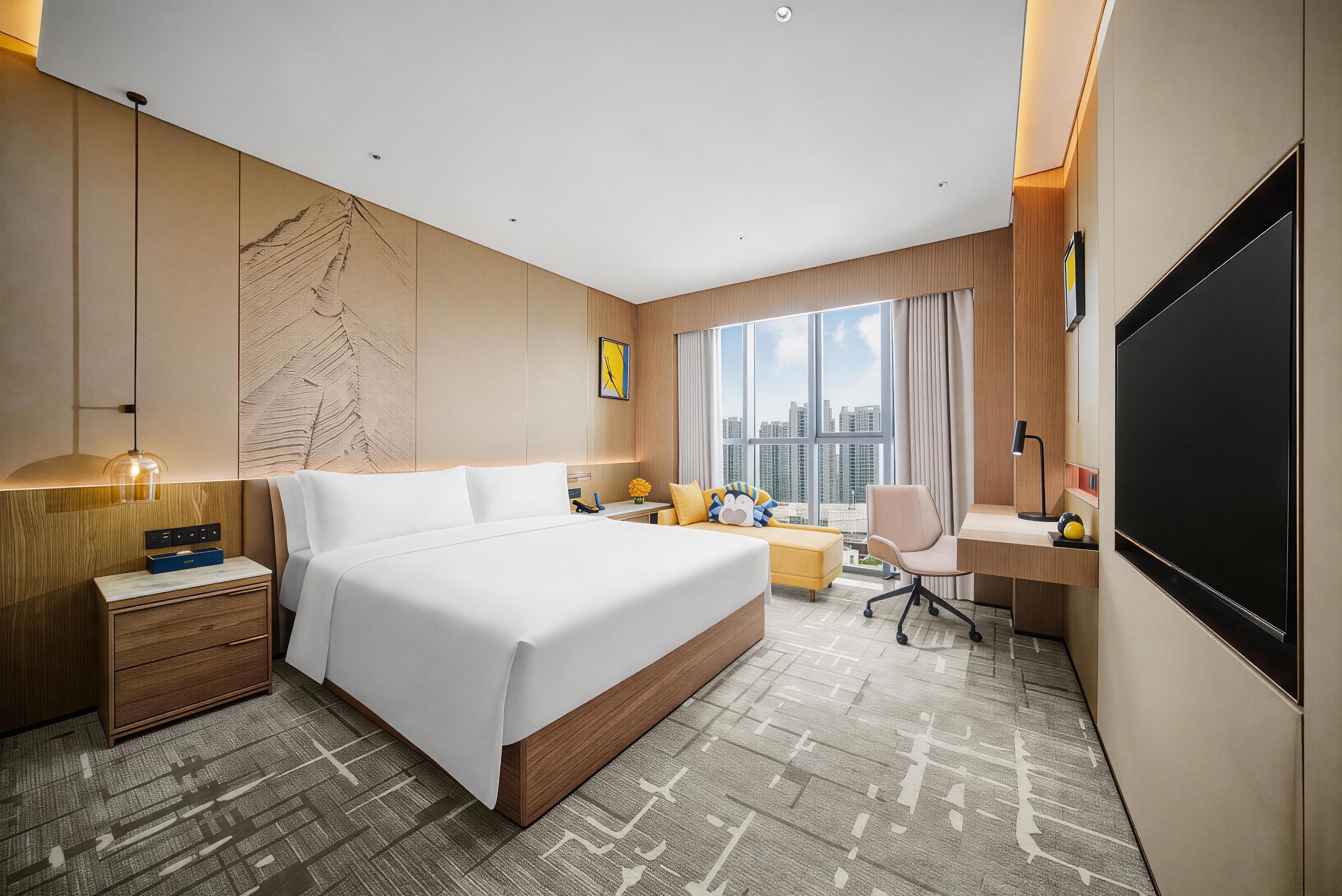 A modern hotel room with a large bed, a desk, a chair, a TV, and a view of the cityscape.