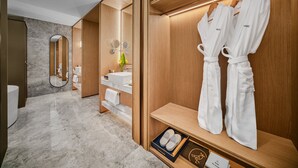 Une salle de bain moderne avec un meuble-lavabo en bois, un grand miroir et deux peignoirs blancs suspendus à une étagère.