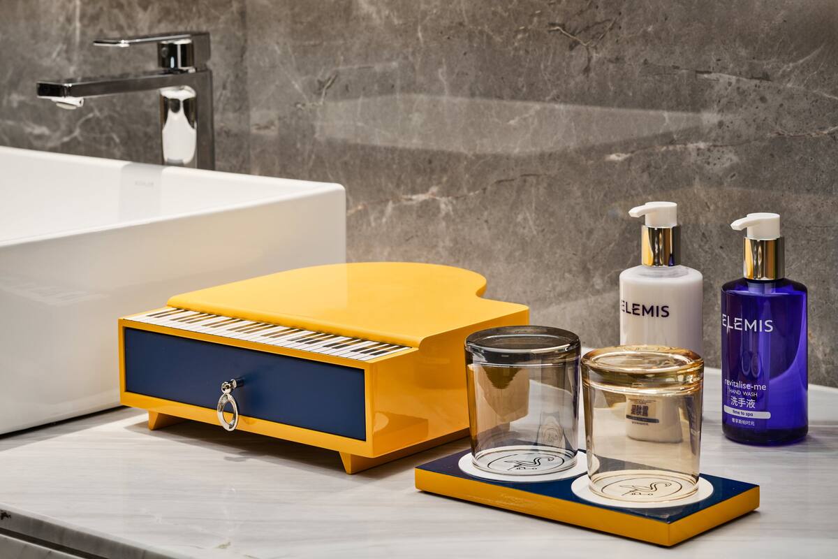 Une salle de bain avec un piano jaune, une bouteille blanche étiquetée « ELEMIS » et une bouteille violette étiquetée « revitalise-moi ».