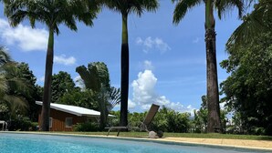 A clear blue pool surrounded by palm trees and a wooden building with a white roof.