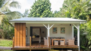A small, single-story house with a covered porch, wooden furniture, and a garden setting.