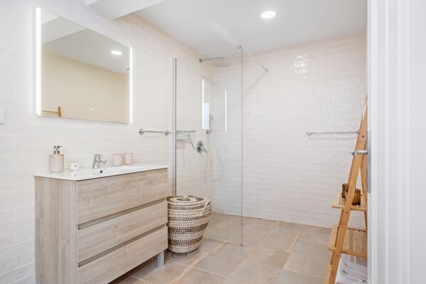 A modern bathroom with a wooden vanity, a large mirror, a glass shower enclosure, and a woven basket.