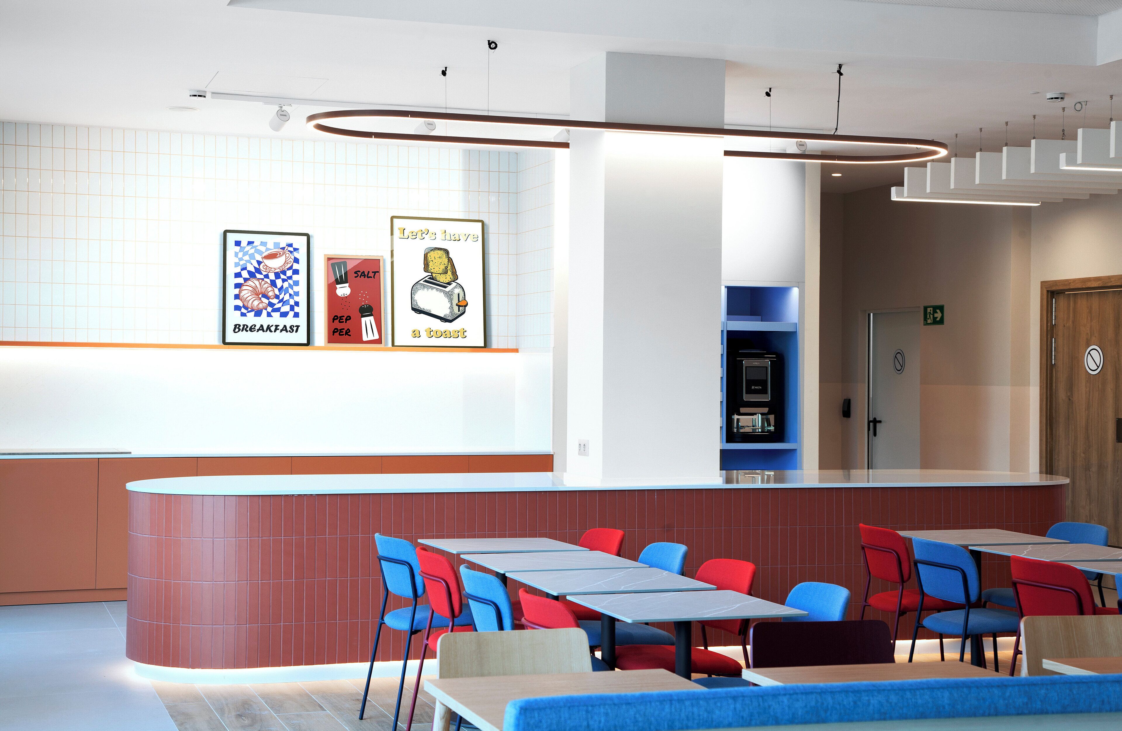 A modern dining area with a counter, multiple tables, and chairs. There are framed pictures on the wall and a wooden door in the background.
