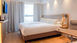 A modern hotel room with a large bed, a bedside table, a chair, a TV mounted on the wall, and a window with curtains. - Holiday Inn Express & Suites Barcelona Sabadell by IHG (Sabadell)