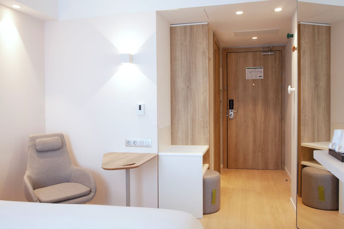 A modern hotel room with a bed, a seating area, a small table, and a wooden door.
