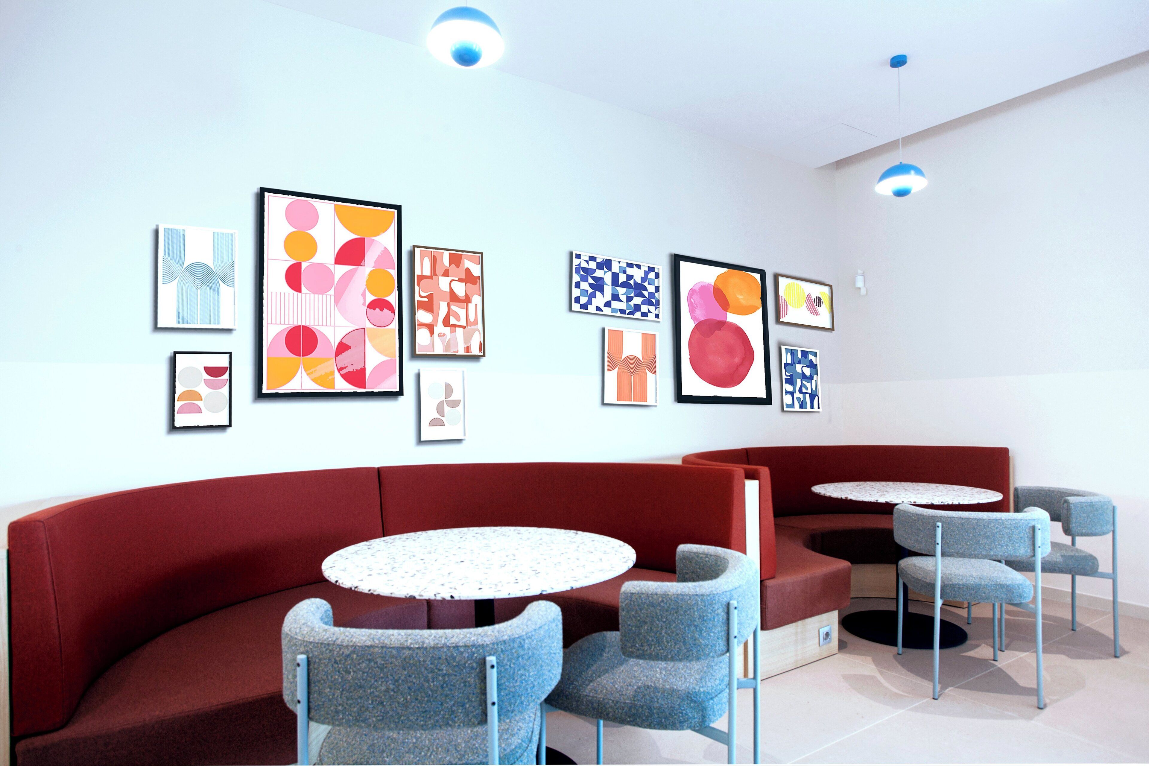 A modern lounge area with a red sofa, round tables, and blue chairs, featuring abstract art on the walls.