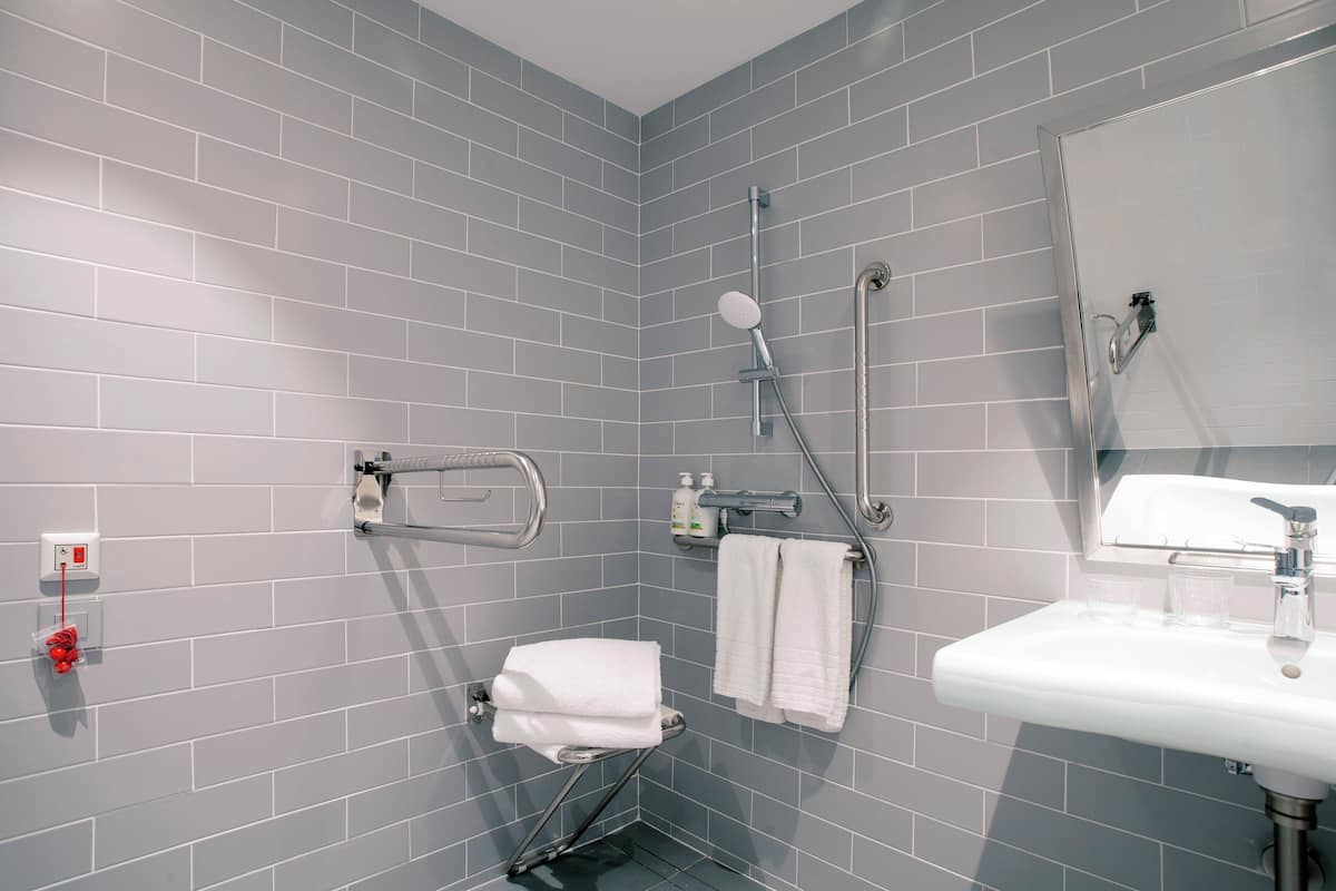 A bathroom with grey tiled walls, a white sink, and a shower with a handheld showerhead.
