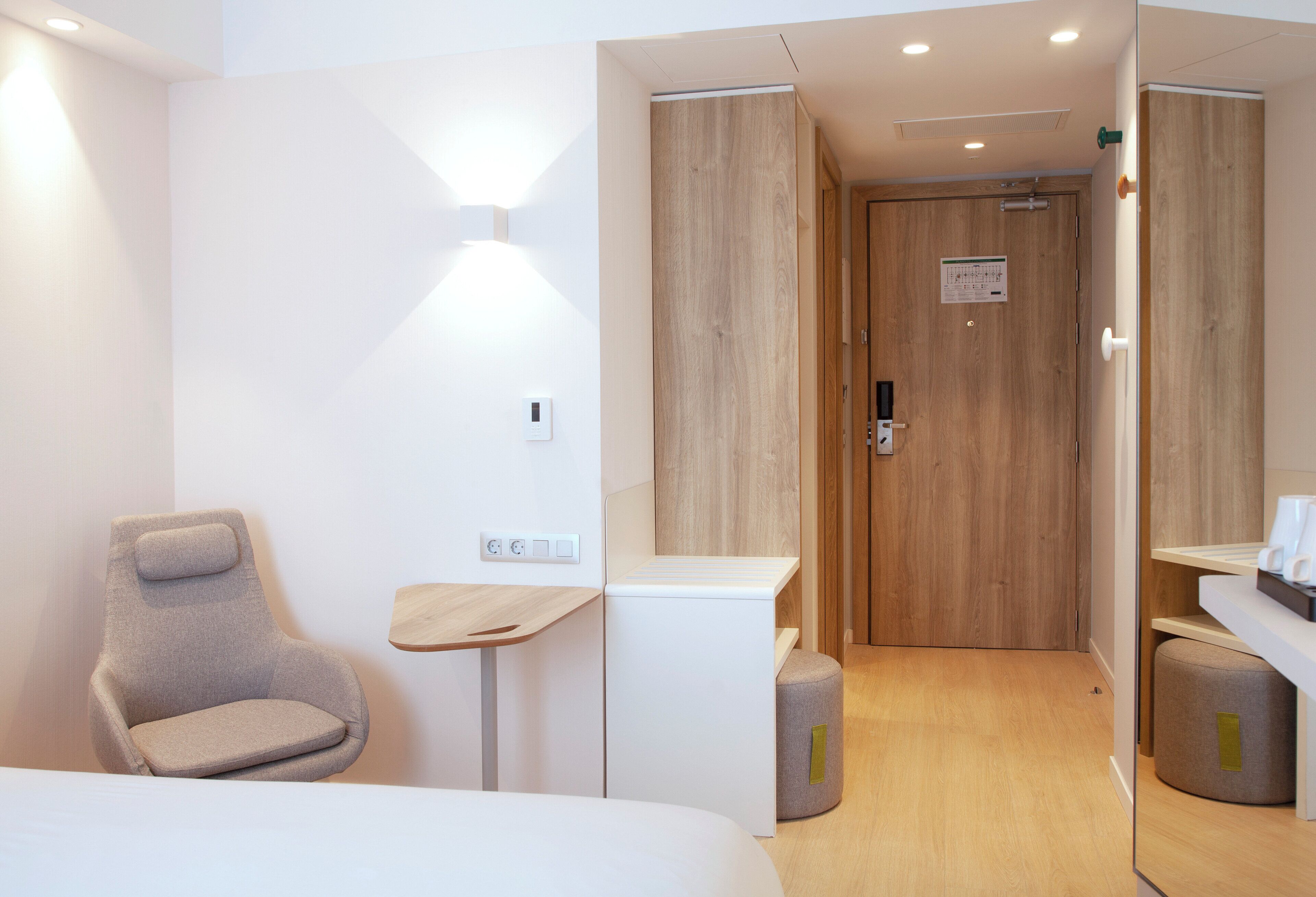 Une chambre d’hôtel moderne comprenant un lit, un coin salon, une petite table et une porte en bois.