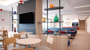 A modern interior with round tables and chairs, a flat-screen TV, and a seating area with colorful cushions.