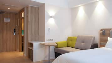 A modern hotel room with a bed, a desk, and a seating area with cushions.