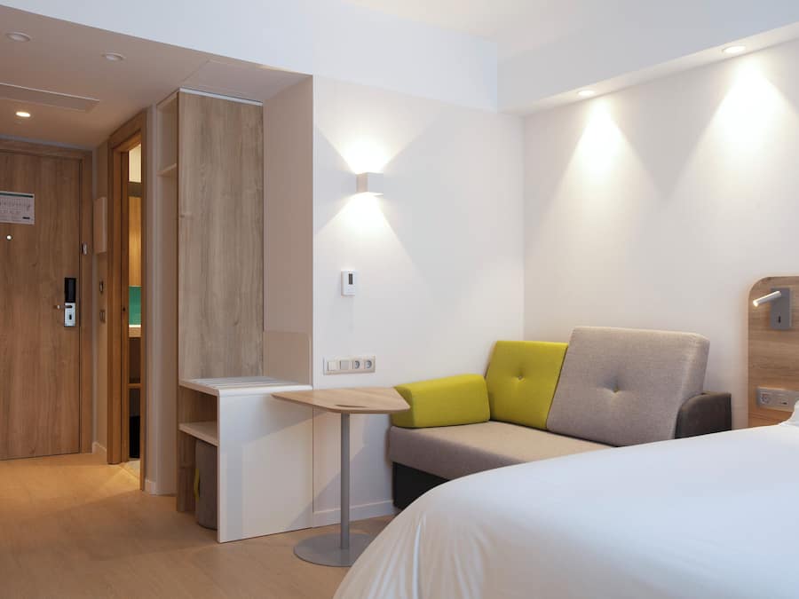 Una habitación de hotel moderna con cama, escritorio y zona de estar con cojines.