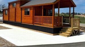 A wooden cabin with a porch, a covered deck, and a small staircase leading up to the entrance. - Alpen Bluffs Outdoor Resort (Gaylord)