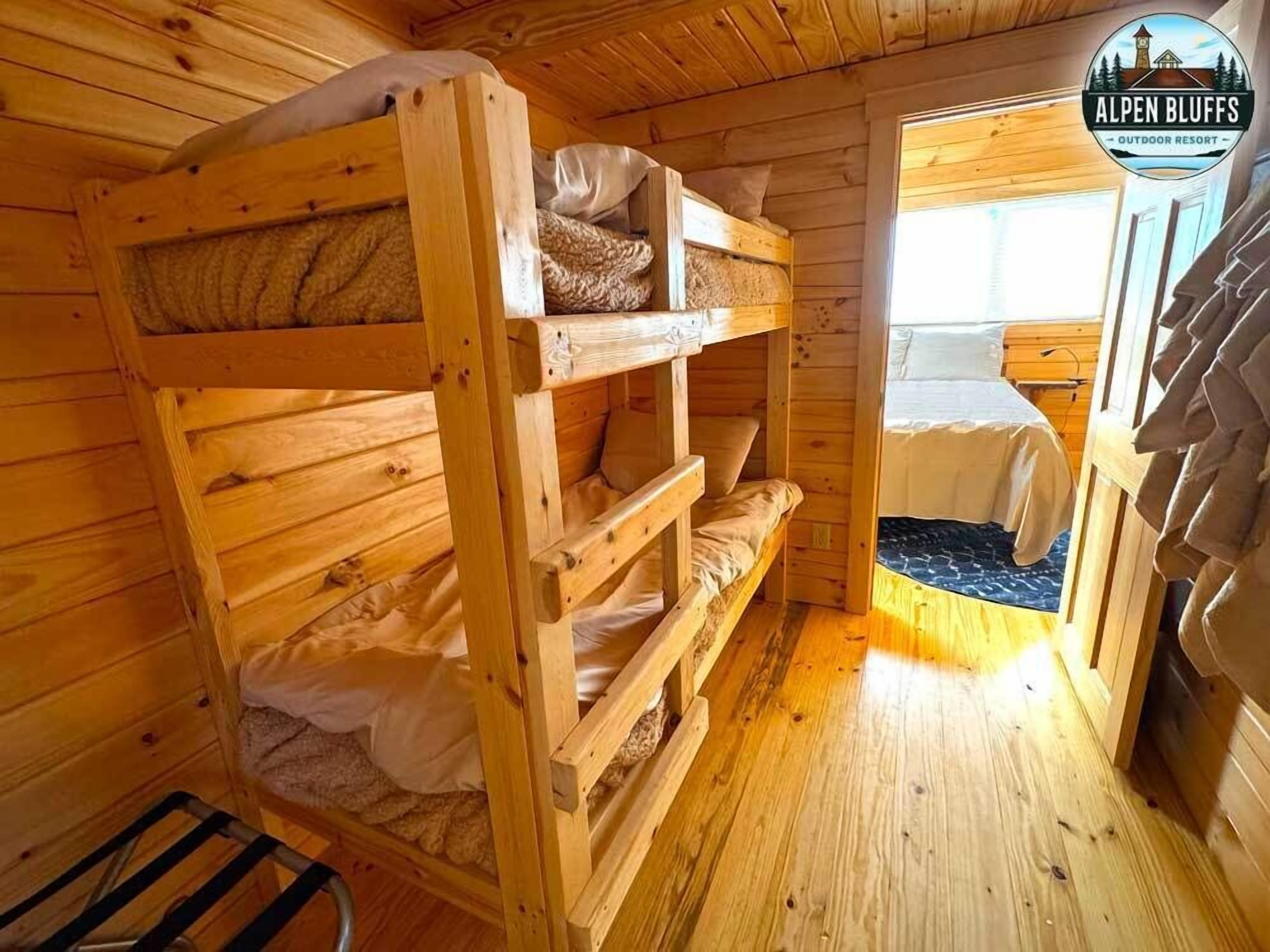 A wooden bunk bed room with a window and a door leading to another room.