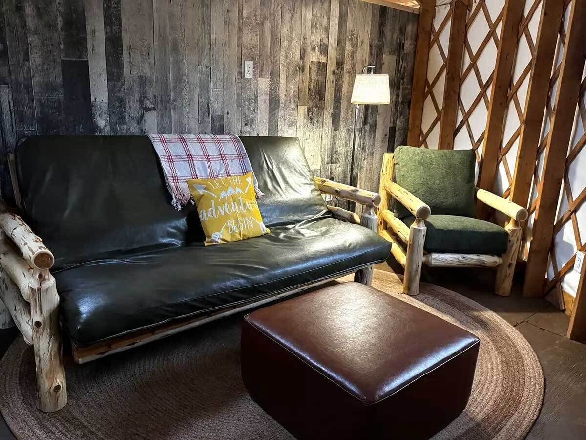 Una habitación acogedora con un sofá de cuero negro, una silla de madera y una mesita redonda.