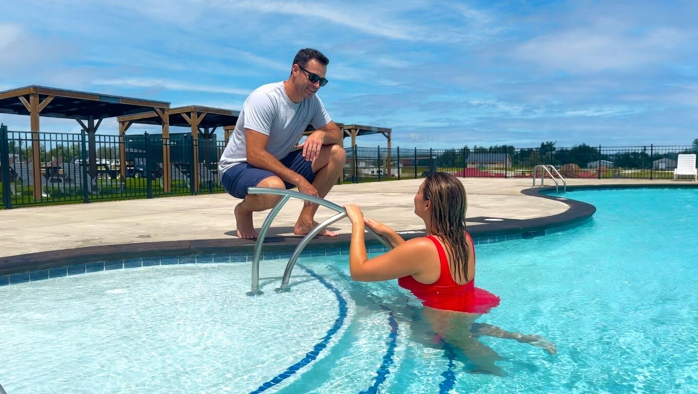 A swimming pool with a metal ladder, a covered seating area, and a clear sky.