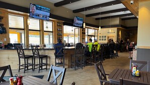 A restaurant with wooden interiors, multiple tables and chairs, and televisions displaying news. - Alpen Bluffs Outdoor Resort (Gaylord)