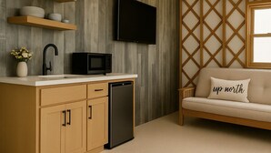 A modern kitchen with wooden cabinetry, a built-in microwave, and a flat-screen TV mounted on the wall. - Alpen Bluffs Outdoor Resort (Gaylord)